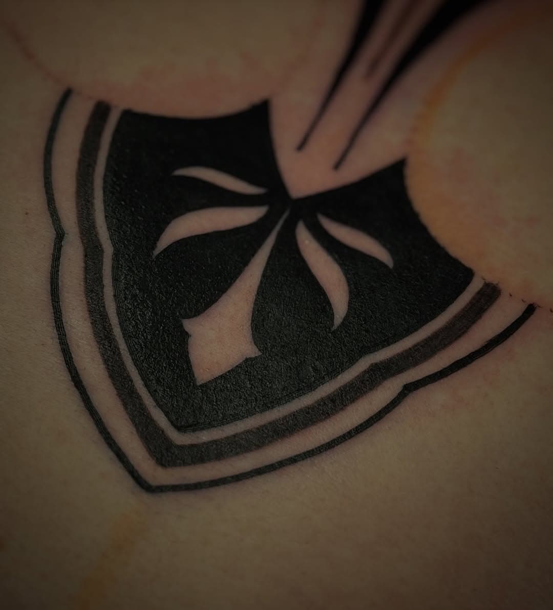 Black geometric tattoo of a lotus flower inside a shield with curved parallel lines creating a dimensional effect
