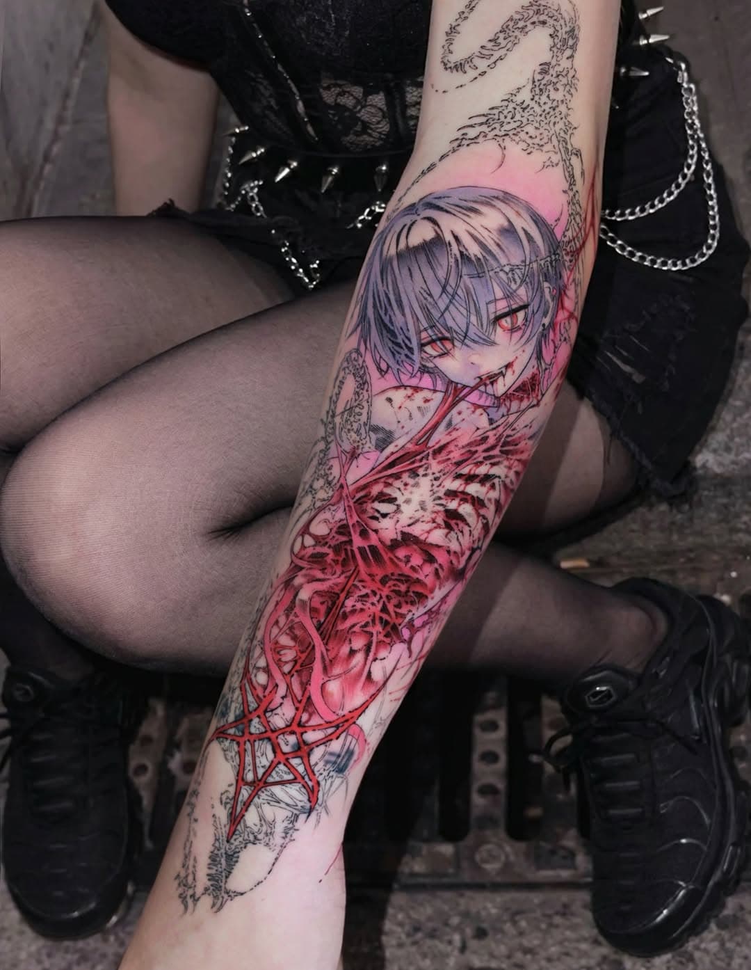 Anime-style character tattoo on forearm with pink and red watercolor effects, skeletal ribcage detail, and decorative linework surrounding the design